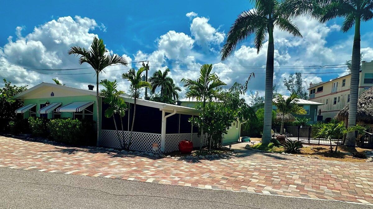 A residential area with a paved walkway, palm trees, and houses with distinct architectural styles.
