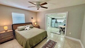 A bedroom with a bed, nightstands, a ceiling fan, and a view into the kitchen. - Turtle Nest Beach Studio - Quick Walk to Beach (Fort Myers Beach)