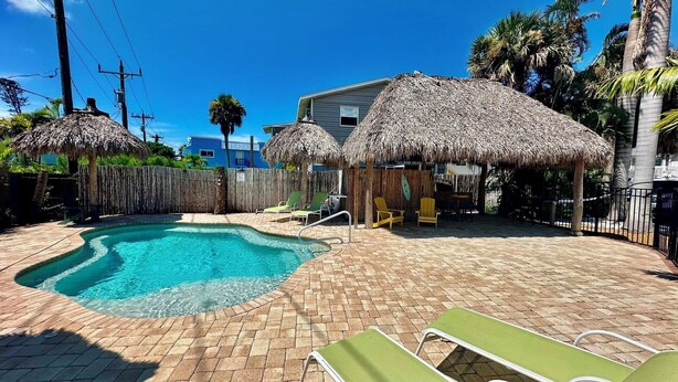 A pool area with a hot tub, lounge chairs, and thatched umbrellas. - Turtle Nest Beach Studio - Quick Walk to Beach (Fort Myers Beach)