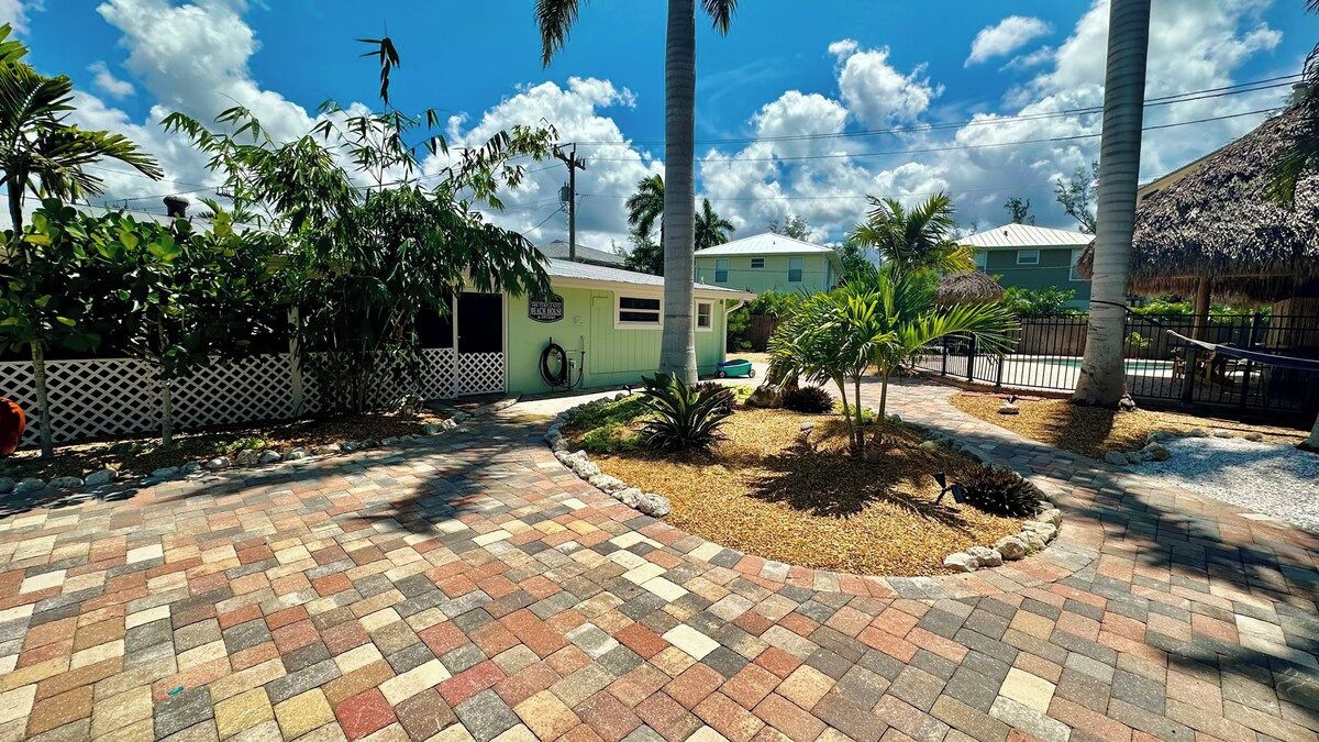 A paved courtyard with a palm tree, a small building, and a thatched-roof structure.