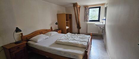 Un dormitorio con cama de madera, mesitas de noche, armario, ventana con cortinas y radiador.
