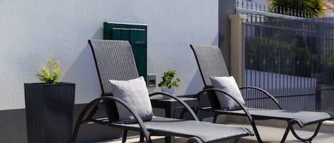 To komfortable liggestole med puder, en potteplante og en flisebelagt terrasse.