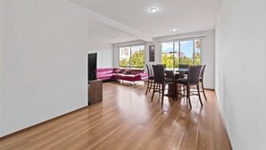 Amplia sala de estar con piso de madera, un sofá rojo, una mesa de comedor con sillas y un televisor.