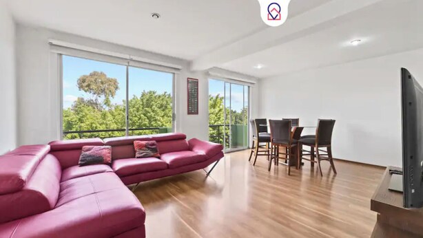 Un salón moderno con un amplio sofá rojo en forma de L, una zona de comedor con sillas de madera y un televisor de pantalla plana sobre un mueble.