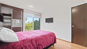 Un dormitorio con cama, armario, televisión y puerta corrediza de vidrio a un balcón.