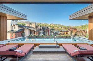 Una piscina al terrat amb gandules, vista d'una muntanya i edificis al fons.