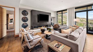 A modern living room with a fireplace, comfortable seating, a flat-screen TV, and large windows offering a view of the outdoors. - One Snowmass Residence Club 403 (Snowmass)
