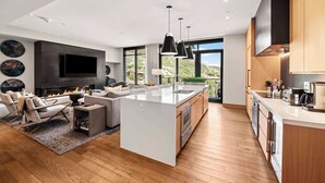 A modern kitchen with a large island, a dining area with a sofa, and a fireplace. - One Snowmass Residence Club 403 (Snowmass)