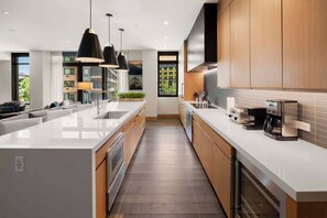 A modern kitchen with a central island, pendant lights, and a view of a building through a window. - One Snowmass Residence Club 406 (Snowmass)