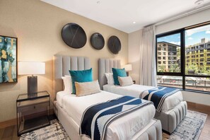 A hotel room with two beds, a large window with a city view, a painting on the wall, and a modern lamp. - One Snowmass Residence Club 406 (Snowmass)