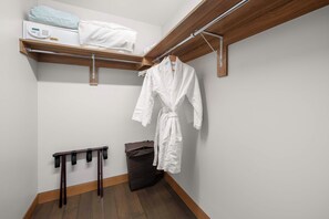 Een hoek van een kamer met een houten plank waarop een wit kussen en een witte badjas liggen. Daaronder staat een zwarte prullenbak en een houten rek met meerdere zwarte banden.