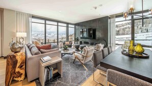 A modern living room with a large TV, comfortable seating, and a view of a snowy landscape.