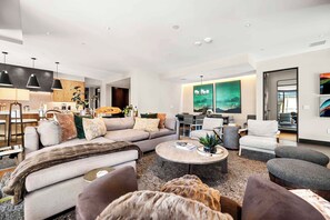 Una sala de estar moderna con un sofá, sillones, una mesa de centro y un comedor, con una cocina al fondo.