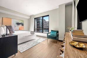 Una habitación de hotel moderna con una cama grande, un escritorio, una silla, un televisor y vistas a la ciudad a través de la ventana.