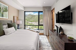 A hotel room with a large bed, a TV, a desk, and a view of a mountainous landscape.