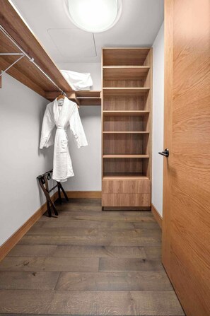 A walk-in closet with wooden shelving, a hanging robe, and a wooden floor.