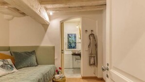 A bedroom with a bed, a small table with a vase and flowers, and a view of a bathroom through an open door. - Stylish Apartment with Spacious Terrace in Florence's Historic Center (Firenze)