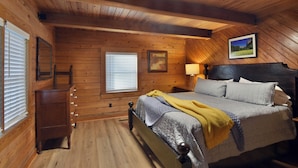A log cabin bedroom with a bed, dresser, and window blinds.