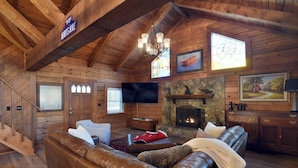 A log cabin interior with a stone fireplace, leather sofas, a television, and wooden walls.