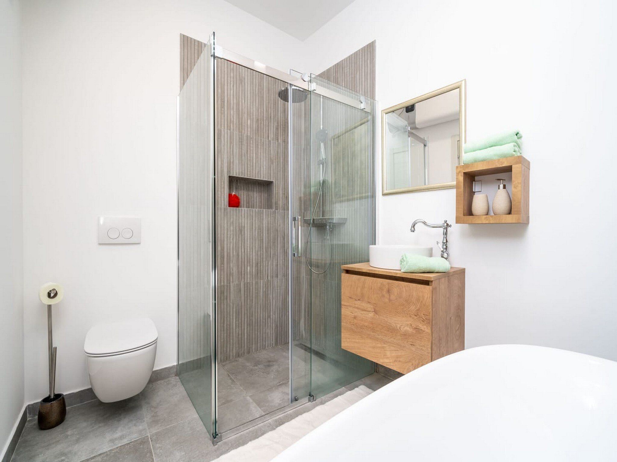 Un baño moderno con ducha de vidrio, tocador de madera, inodoro blanco y espejo sobre el tocador.