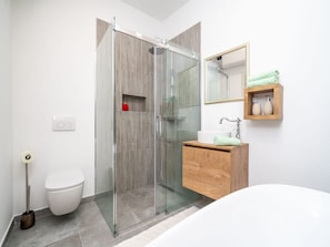 Un baño moderno con ducha de vidrio, tocador de madera, inodoro blanco y espejo sobre el tocador.