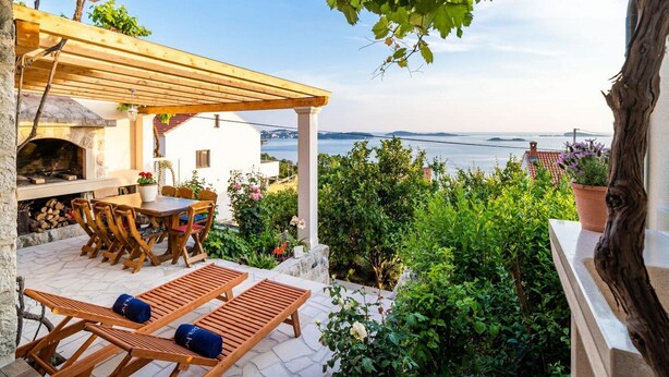 A patio with a stone fireplace, wooden furniture, and a view of the sea. - Apartment Fortuno (Zupa dubrovacka)