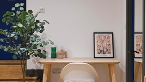 Un espacio de trabajo con escritorio, silla, planta en maceta y cuadro colgado en la pared.