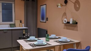 Un comedor moderno con una mesa dispuesta para dos, una cocina al fondo y una lámpara fijada a la pared.