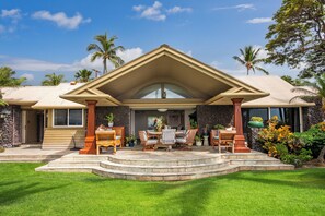 Een huis met een stenen gevel, een overdekt terras met buitenmeubilair en uitzicht op palmbomen.