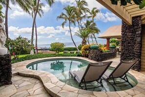 A pool area with lounge chairs, palm trees, and a stone wall. - Puako Beach Luxury Oceanfront Home- 3 Guest Suites (Waimea)