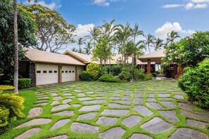 Zona residencial com um caminho de pedra, palmeiras e uma garagem.