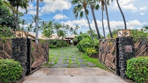 A gated entrance with stone steps leading to a building, surrounded by palm trees and greenery. - Puako Beach Luxury Oceanfront Home- 3 Guest Suites (Waimea)
