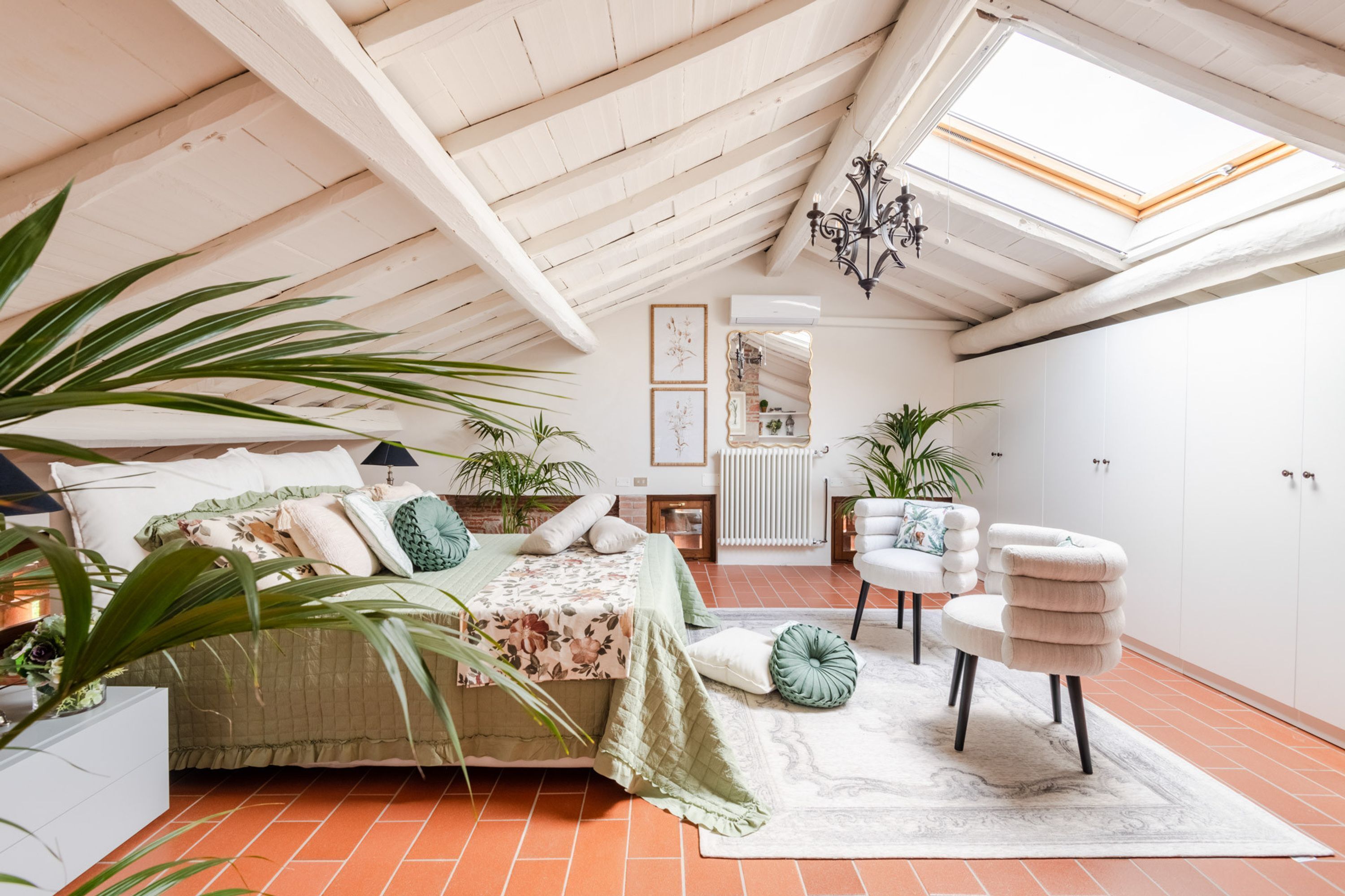 Une chambre confortable située sous les toits, avec un lit, un coin salon et des plantes en pot.