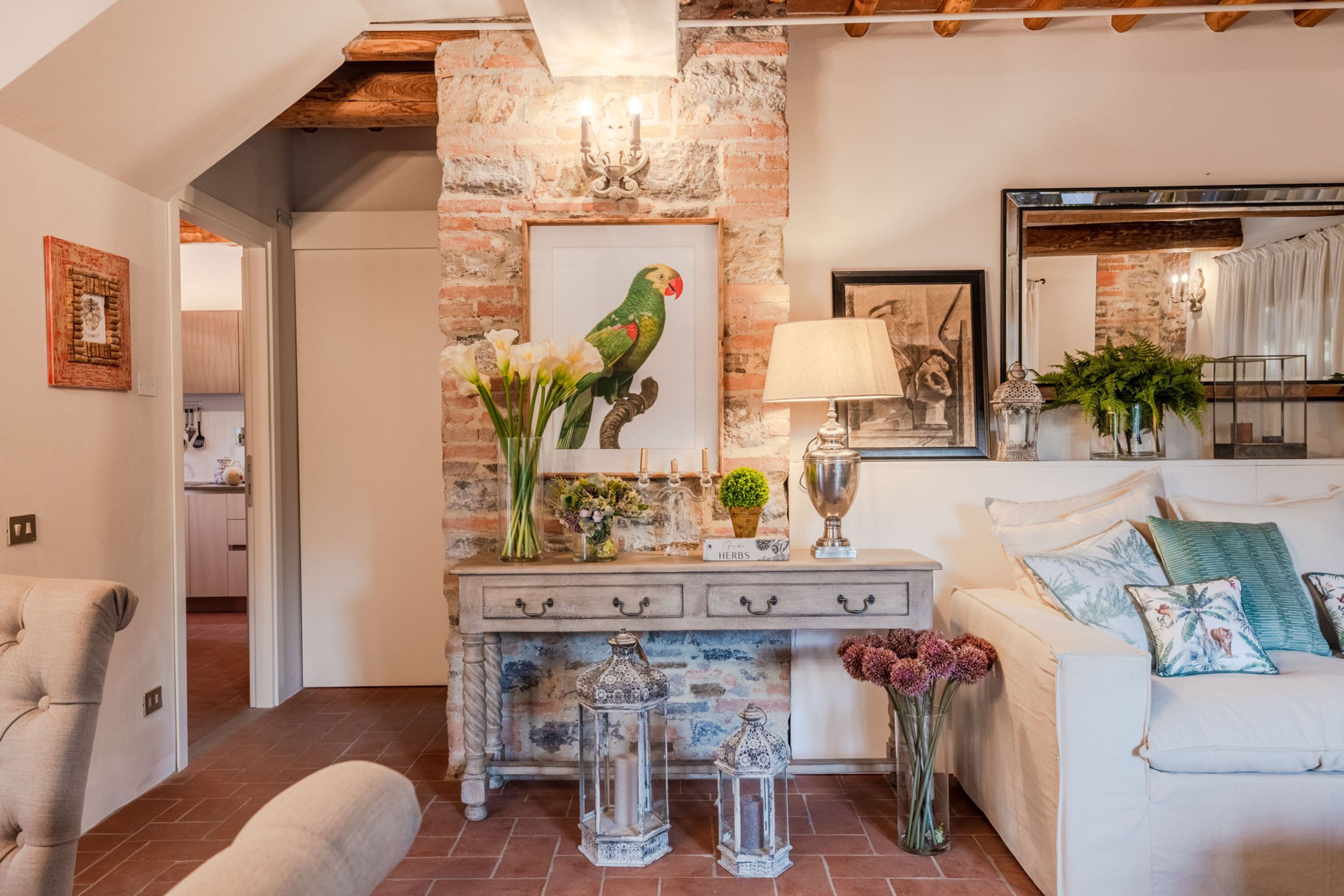 Un salon avec un mur en briques, un canapé blanc, une table basse et un tableau représentant un perroquet.