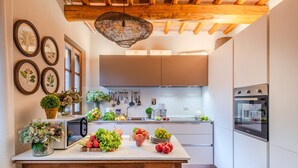 A modern kitchen with white cabinets, a wooden ceiling, and a central island with fresh produce and decorative plants. - Valle del Sole Winery Farmhouse (Lucca)