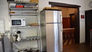 Et køkken med et rustfrit stål køleskab, en mikrobølgeovn og diverse køkkenredskaber på hylder.