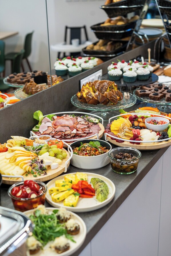 Een buffet met diverse gerechten, waaronder vleeswaren, kazen, fruit en desserts.