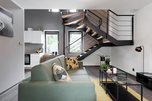 Un espacio habitable moderno con una escalera, un sofá, una mesa de centro y una zona de cocina.