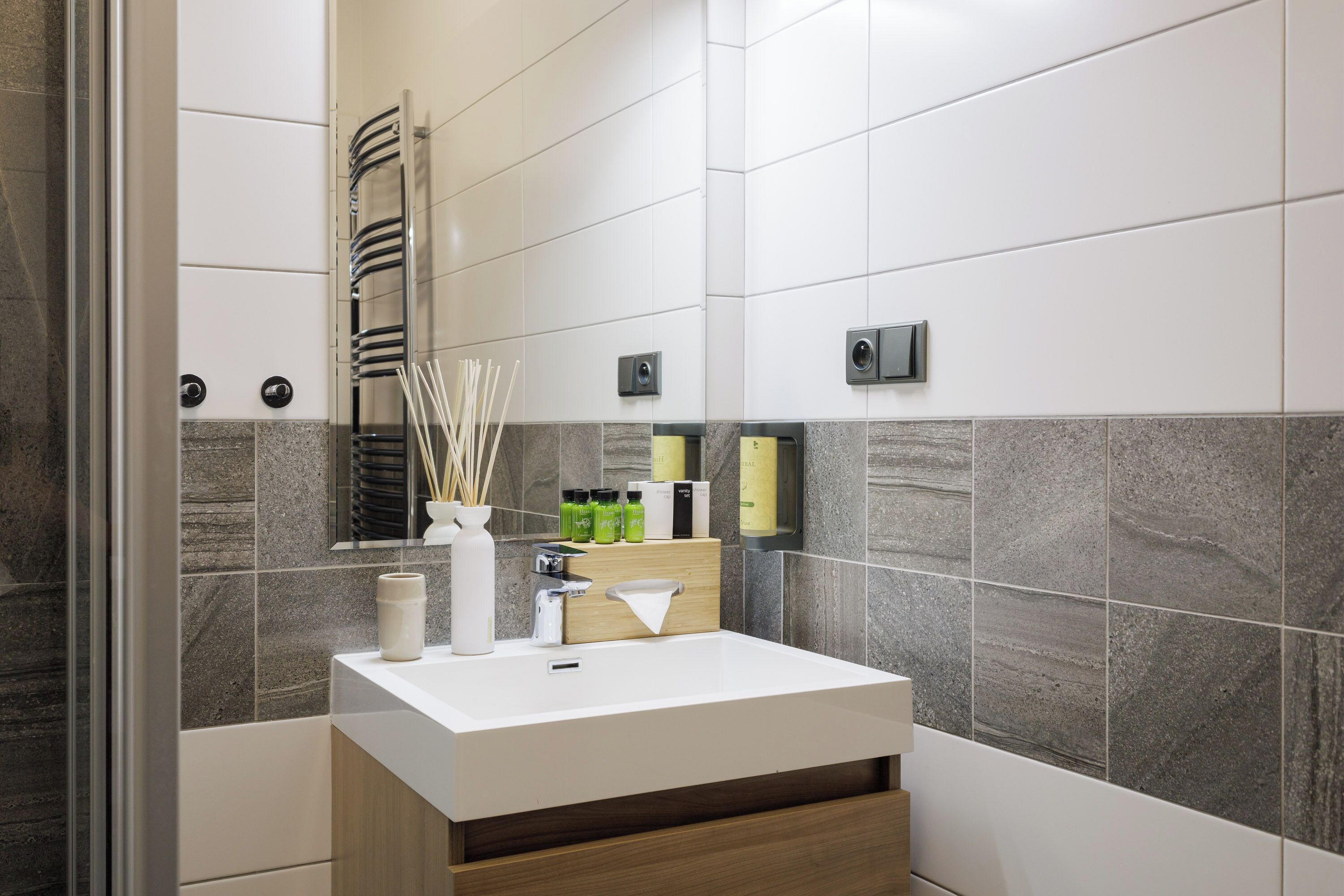 A modern bathroom with a white sink, a mirror, a towel rack, and a shower area.