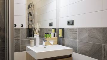 A modern bathroom with a white sink, a mirror, a towel rack, and a shower area.