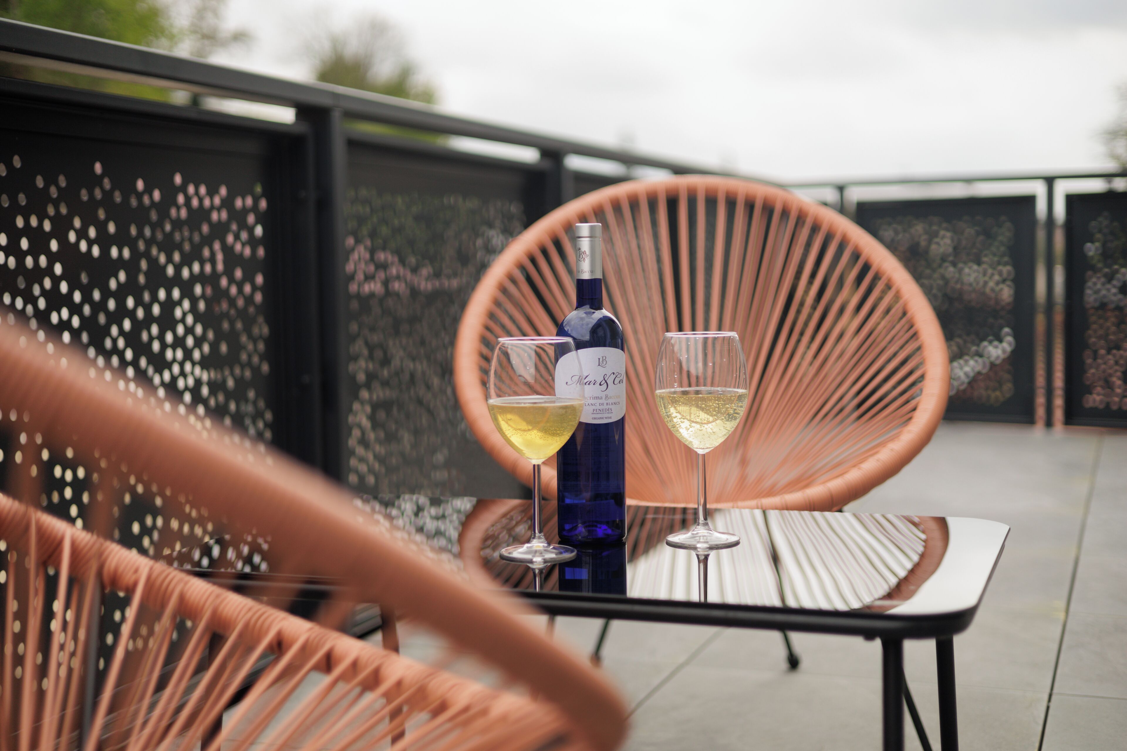 A table with a bottle of wine and two glasses on a balcony.