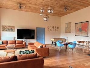 A living room with a wooden ceiling, a flat-screen TV, orange sofas, a coffee table, a blue chair, and a table with a board game. - House for 18p "la Foresterie" 6 bedrooms, 7 bathrooms (Échandelys)