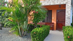 A building with a stone facade, a wooden door, and a well-maintained garden with various plants and shrubs. - Süßes, Privates Bungalow mit Garden Nahe Manuel Antonio in Einer Ruhigen Gegend (San Martin Quepos)