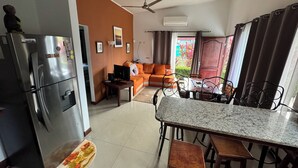 A modern kitchen with a refrigerator, dining table, and bar stools. There is a sofa and a TV in the living area. - Süßes, Privates Bungalow mit Garden Nahe Manuel Antonio in Einer Ruhigen Gegend (San Martin Quepos)