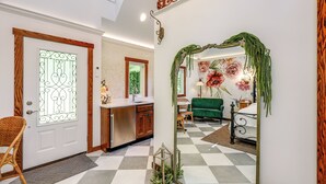 Een modern interieur met een geruite vloer, een houten deur met ruit en een groene bank, met een spiegel die de kamer weerspiegelt.
