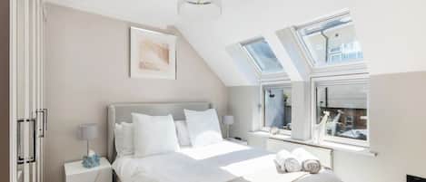 A bedroom with a bed, bedside tables, a chandelier, and skylights.