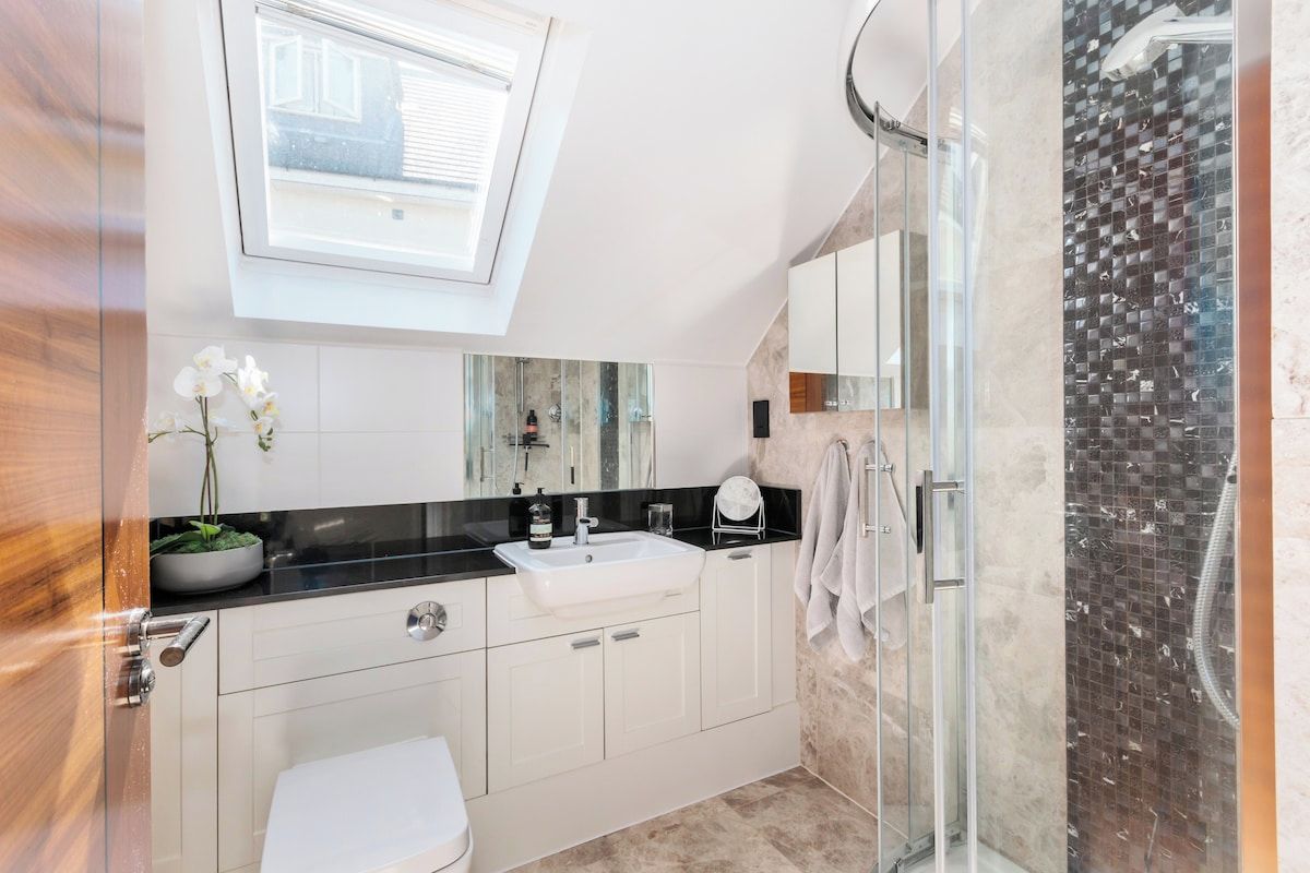 Une salle de bain moderne dotée d’un puits de lumière, d’une douche en verre et d’un lavabo blanc.