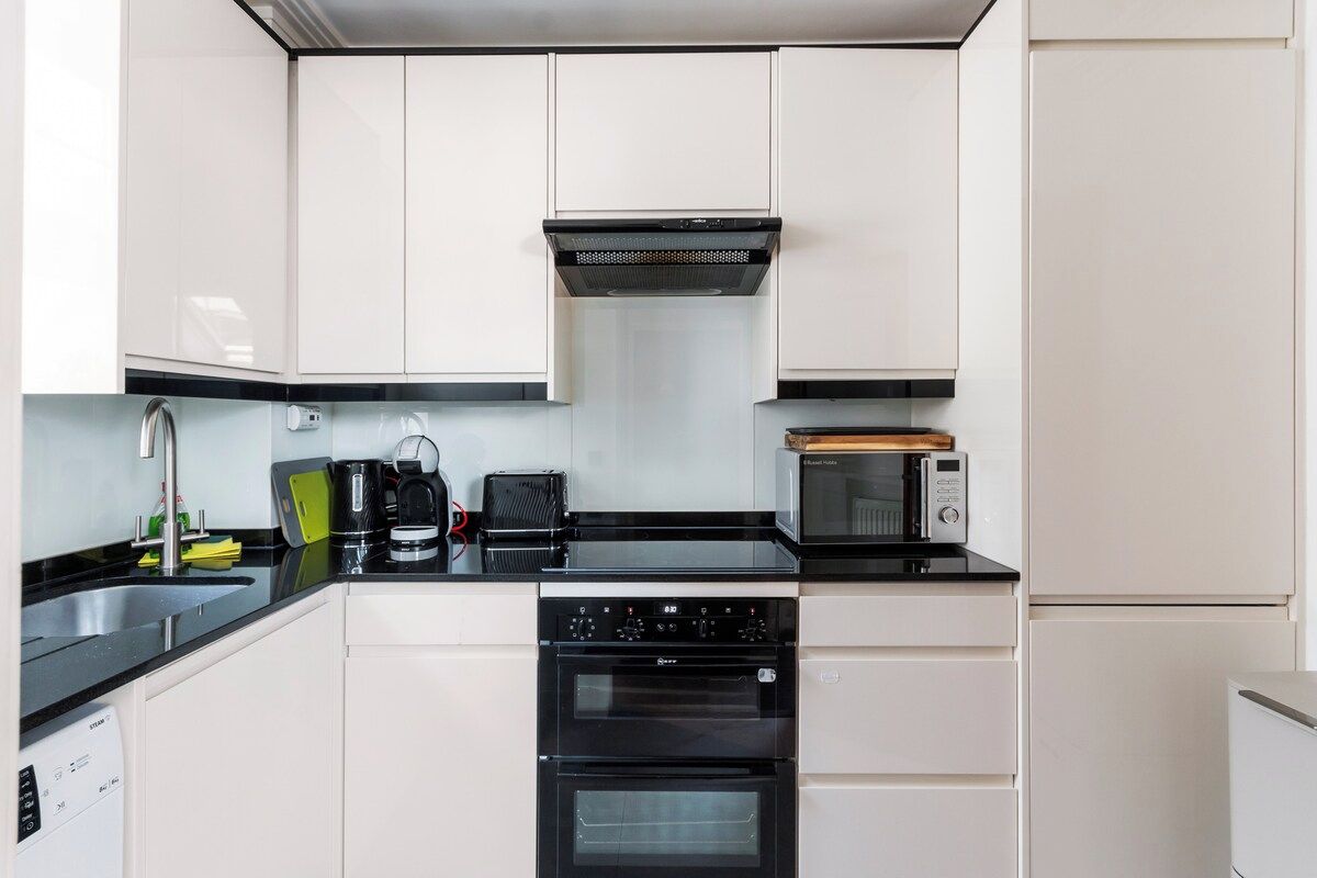 A modern kitchen with white cabinets, a black countertop, a built-in oven, a microwave, and a coffee maker.