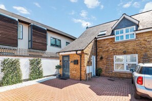 A residential property with a brick house, a car parked in the driveway, and a small garden area. - Weybridge - 2 Bed - parking (Weybridge)