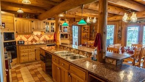 A rustic cabin-style kitchen with wooden cabinets, granite countertops, and a large island with a sink. - Redstone, a one-of-a-kind, luxurious 7200 sq. ft. impressive Lakeside log home (Land O' Lakes)